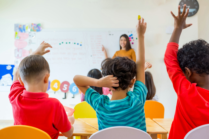 Preschool kid raise arm up to answer teacher question on whiteboard in classroom,Kindergarten education concept.