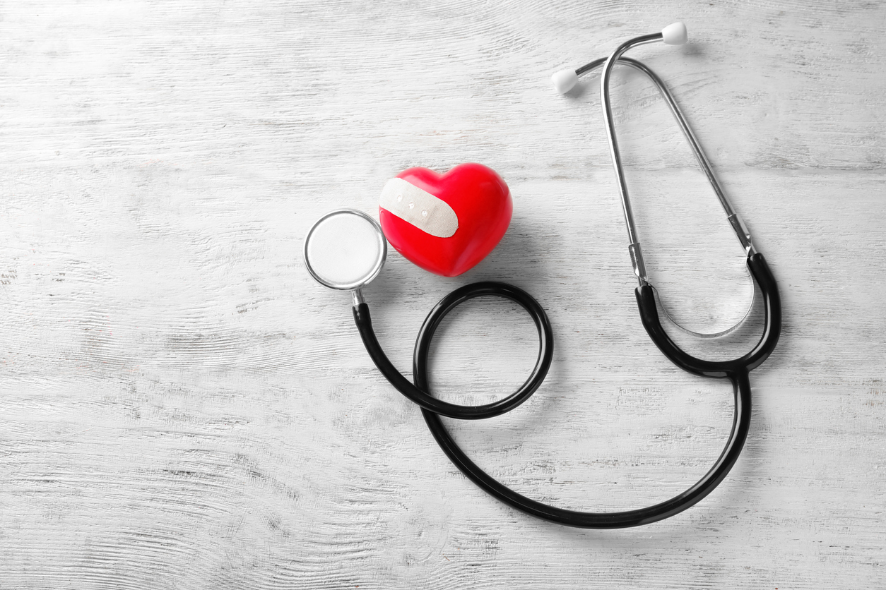 Red heart with medical plaster and stethoscope on wooden background. Health care concept