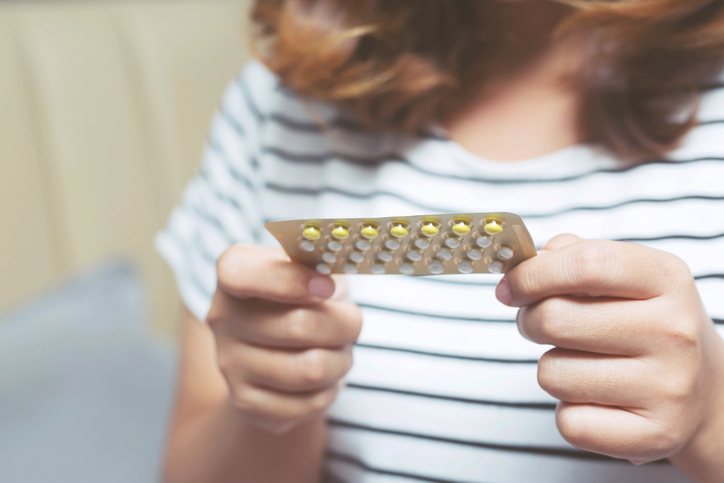 Woman hands opening birth control pills in hand on the bed in the bedroom. Eating Contraceptive Pill.