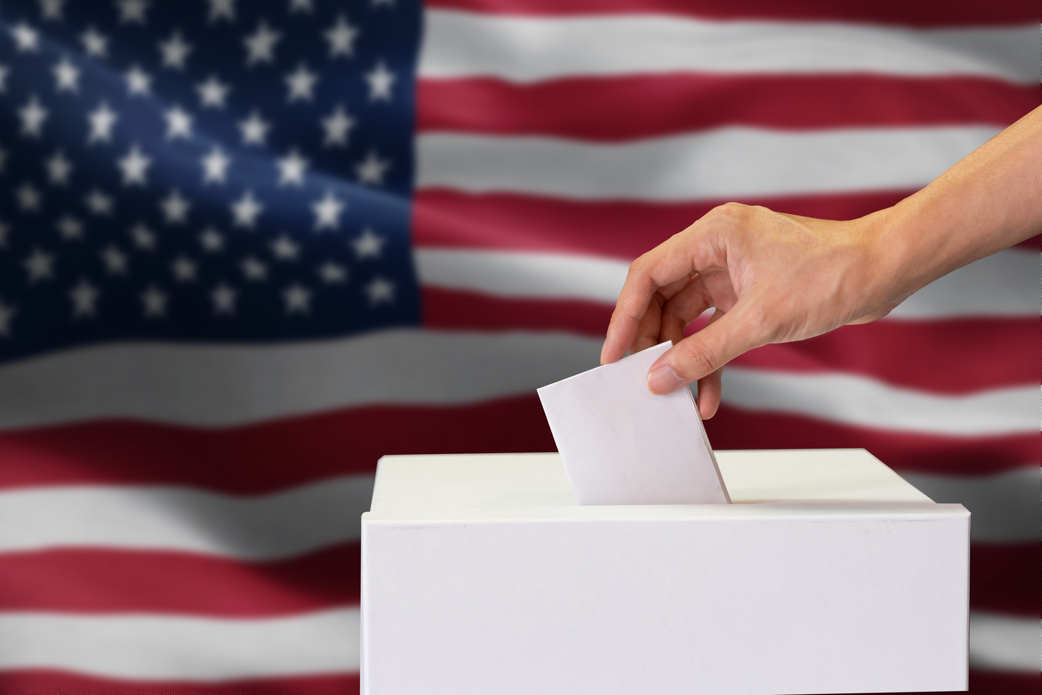 Close-up of man casting and inserting a vote and choosing and making a decision what he wants in polling box with United States flag blended in background.
