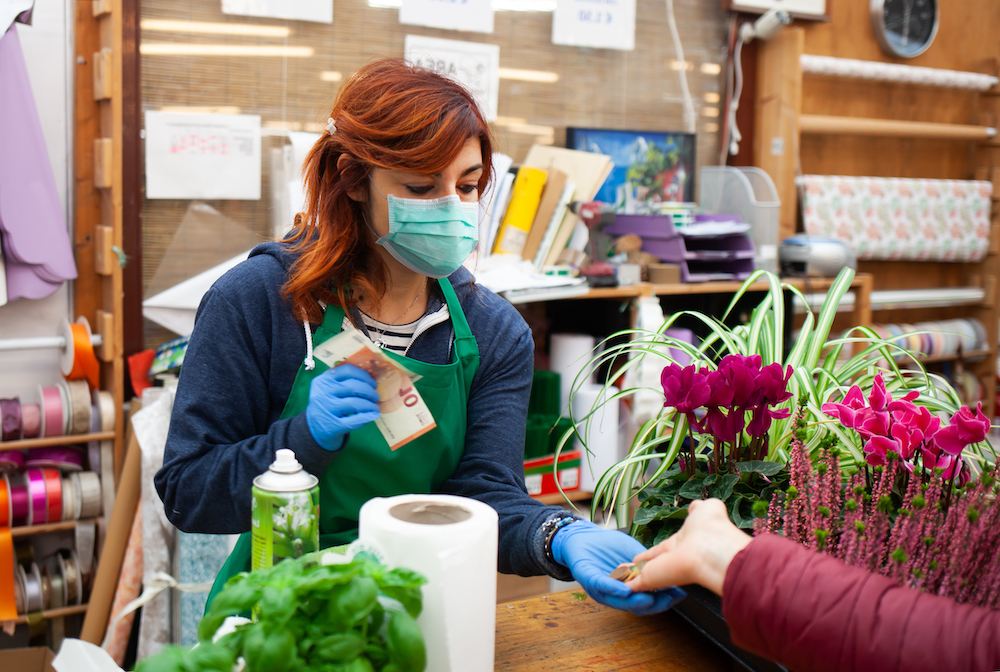 Florist in a nursery receives a payment from a customer wearing a mask and gloves due to the coronavirus covid-19.