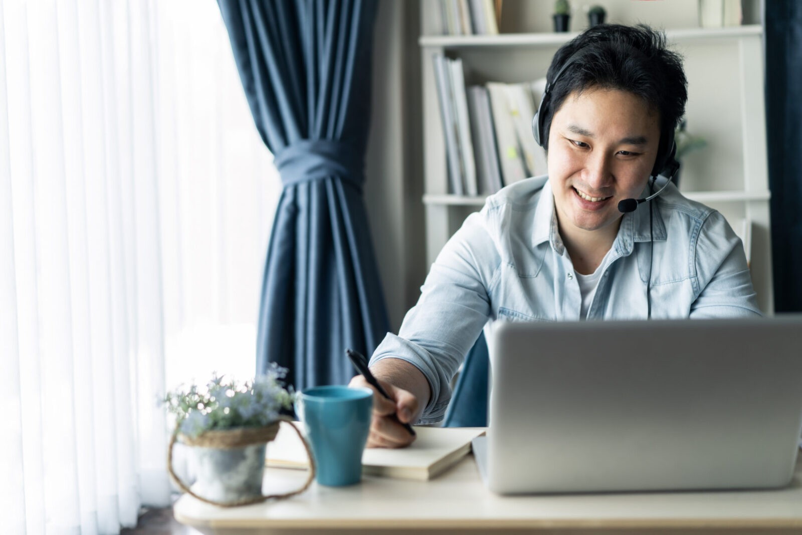 Man working from home, smiling at his computer and using headset