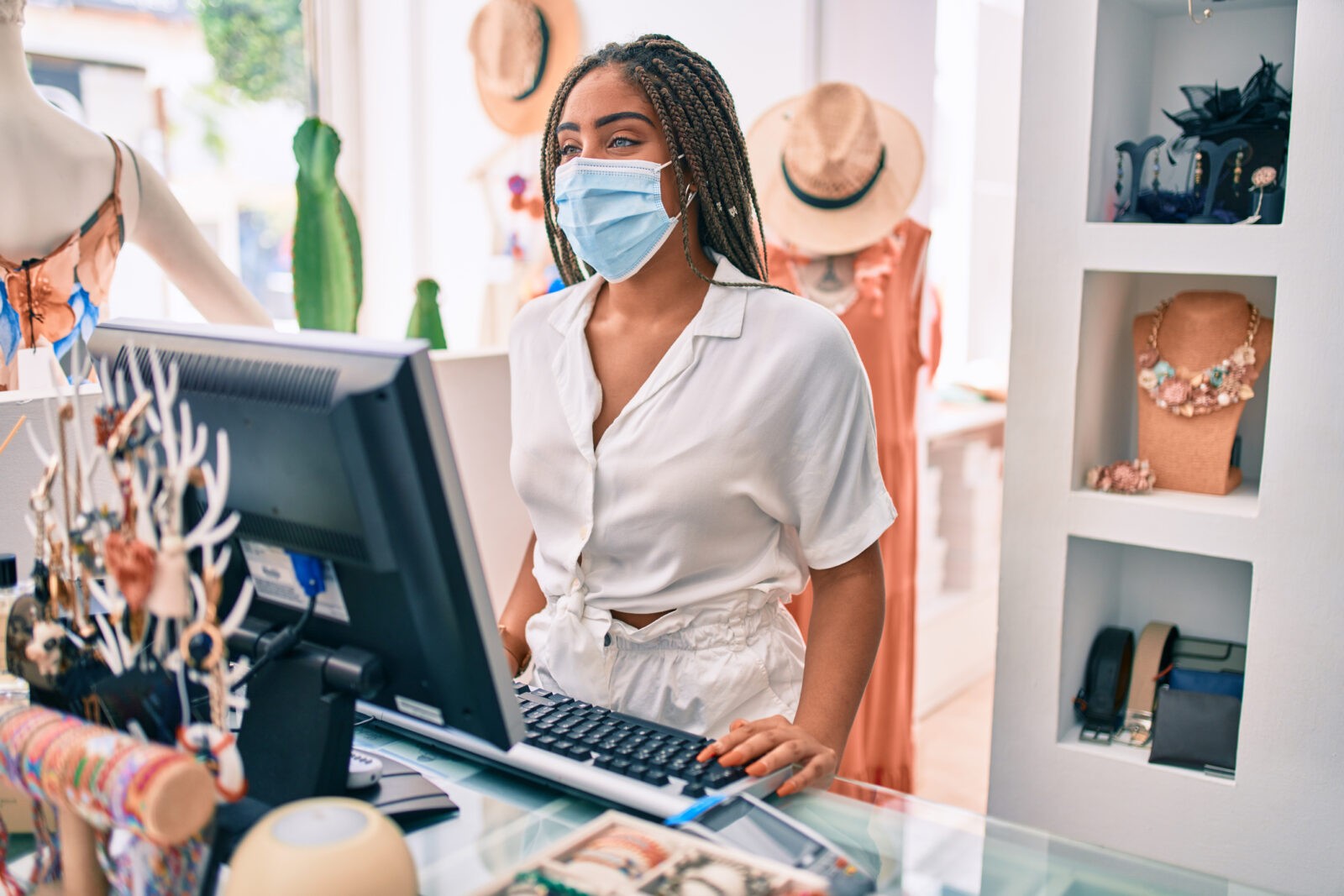 Young African American woman smiling happy working at the till wearing coronavirus safety mask at retail shop