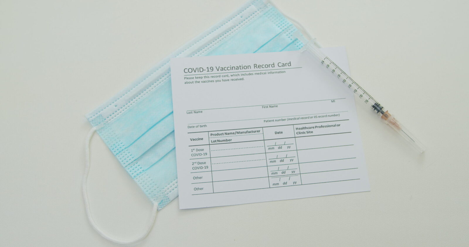 Medical mask and COVID-19 vaccine on vaccination record card approved by CDC with corona virus vaccine vials. White background.