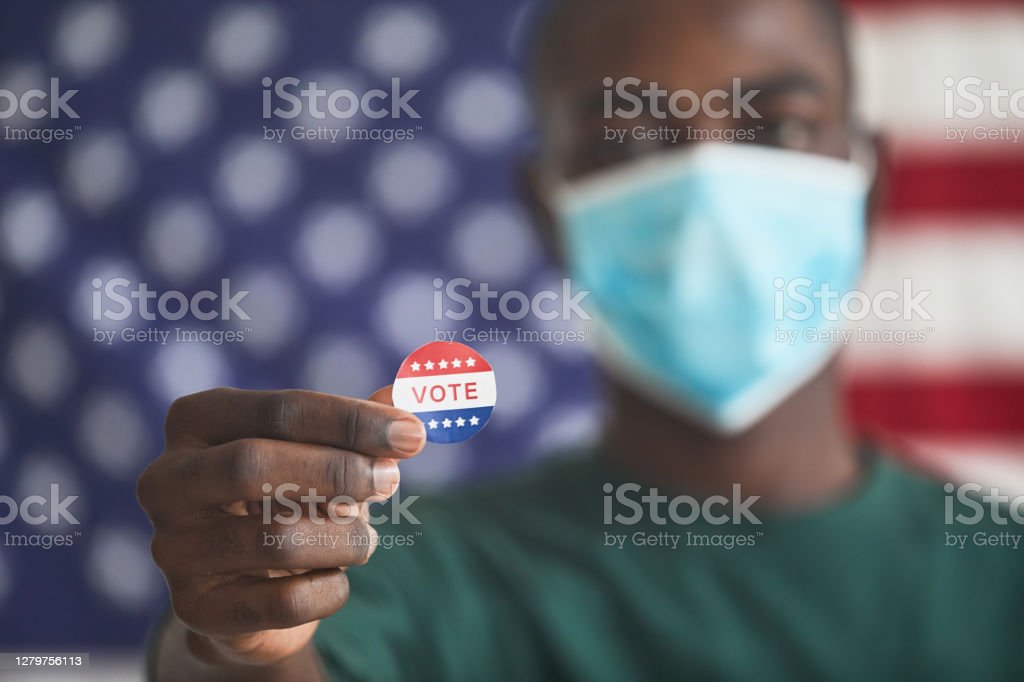 Close-up of African man in mask holding sticker with word Vote
