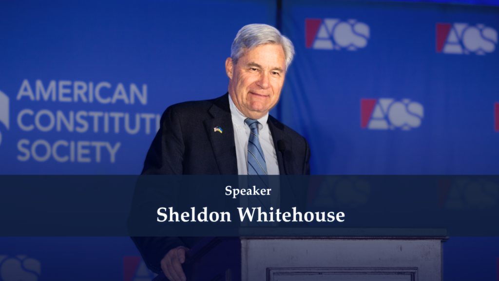 Senator Sheldon Whitehouse delivering a speech at a podium with a blue backdrop showing American Constitution Society logos.