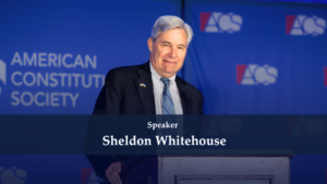 Senator Sheldon Whitehouse delivering a speech at a podium with a blue backdrop showing American Constitution Society logos.